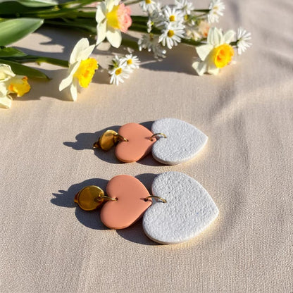 Boucles d’oreilles Thalia en forme de cœurs, avec un cœur en pâte polymère blanc granite effet velours et un cœur en pâte polymère rose poudré recouvert de résine, montés sur acier doré.