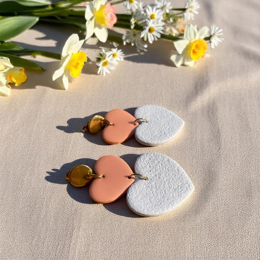 Boucles d’oreilles Thalia en forme de cœurs, avec un cœur en pâte polymère blanc granite effet velours et un cœur en pâte polymère rose poudré recouvert de résine, montés sur acier doré.