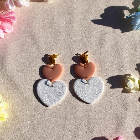 Boucles d’oreilles Thalia en forme de cœurs, avec un cœur en pâte polymère blanc granite effet velours et un cœur en pâte polymère rose poudré recouvert de résine, montés sur acier doré.