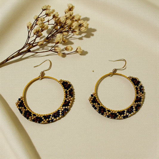Boucles d’oreilles Naya tissées à la main en perles Miyuki Delica dorées, cognac et noires, motif léopard sur créole dorée.